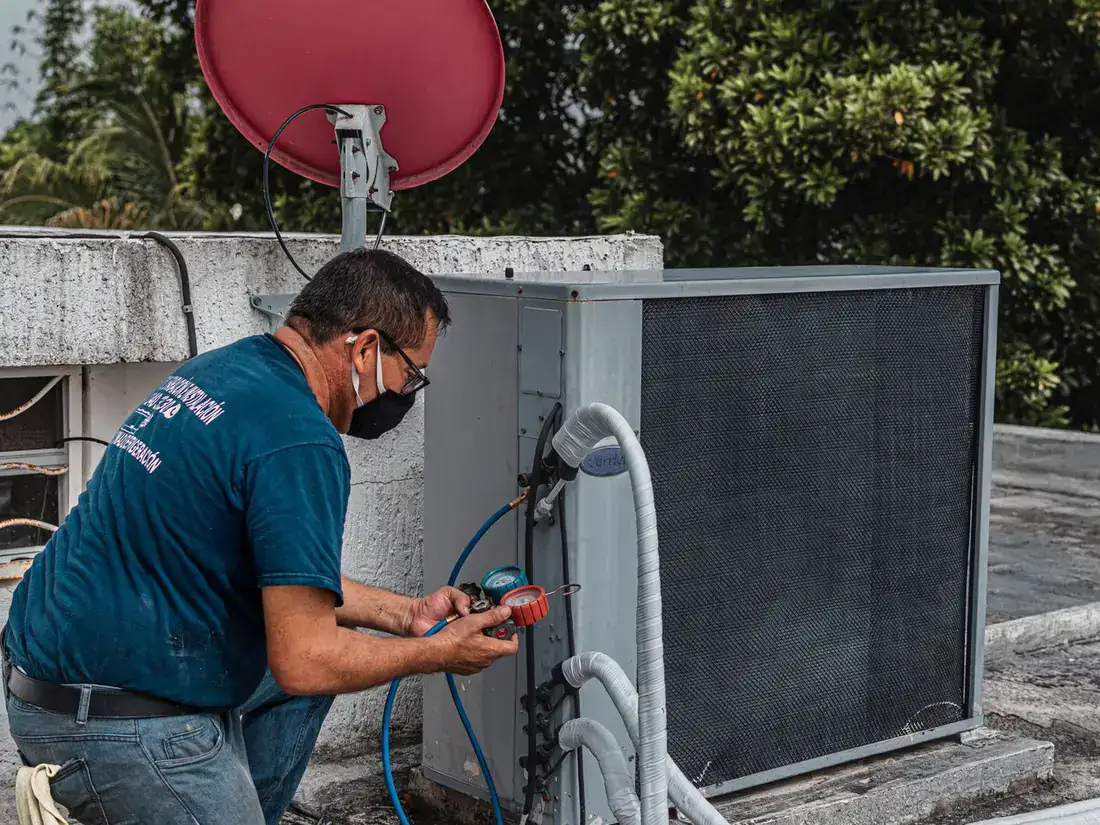 Un técnico de climatización revisando los manómetros de una unidad de aire acondicionado exterior